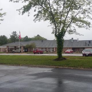 A view of a building surrounded by trees and parked cars under an overcast sky.