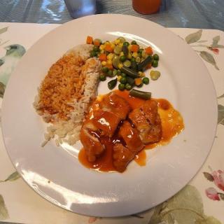 A plate of food featuring rice, mixed vegetables, and saucy meat.