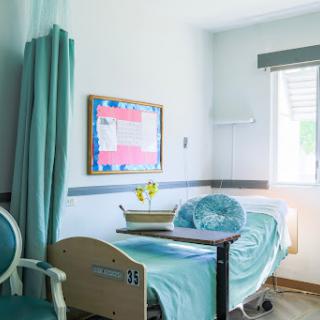 A serene hospital patient room featuring a bed, chair, and a window filled with natural light.
