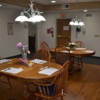 A well-lit dining area with wooden tables and chairs, adorned with flower centerpieces.