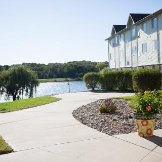 A sunny view of a lakeside apartment with a landscaped sidewalk and blooming flowers.