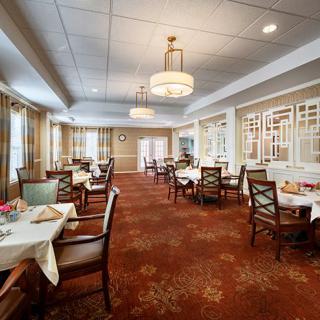 An elegant dining room with neatly arranged tables and chairs, illuminated by chandeliers.