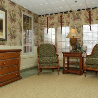 A cozy living room with patterned armchairs, a wooden side table, and a lamp by the window.