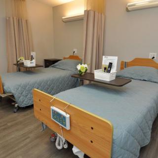 A hospital room with two beds, each equipped with adjustable trays and personal items.