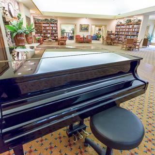 A grand piano in a library with bookshelves and a sitting area.