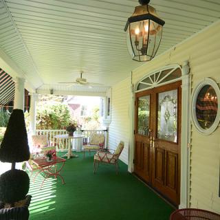 A charming covered porch featuring wooden doors, outdoor seating, and a ceiling fan.