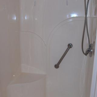 A bathroom shower with a grab bar and handheld showerhead.