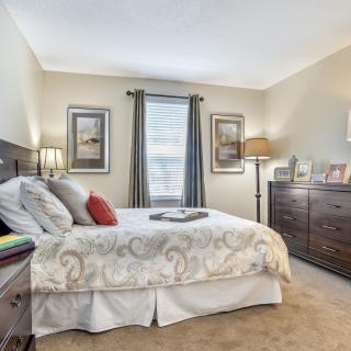 A cozy bedroom with a neatly made bed, dresser, and warm lighting.