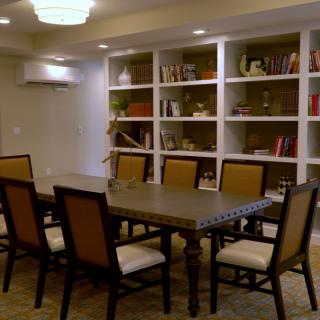A well-lit conference room with a large table surrounded by chairs, and bookshelves in the background.