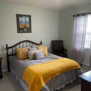 A cozy bedroom with a neatly made bed featuring a yellow blanket and several pillows, complemented by soft lighting from a window.