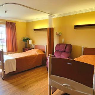 A well-lit hospital room featuring two beds and a comfortable seating area.