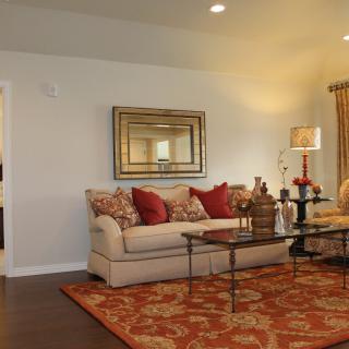 A cozy living room featuring a beige sofa with red and patterned pillows, a glass coffee table, a decorative rug, and a wall mirror.