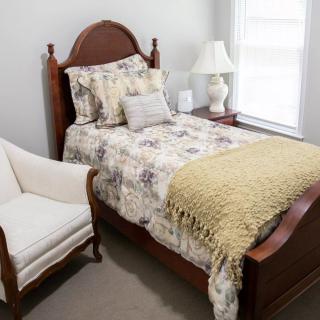 A cozy bedroom with a single bed adorned with floral bedding, an armchair, and a lamp by the window.