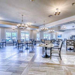 A spacious dining area with elegant chandeliers, featuring neatly arranged tables and chairs on wooden flooring.