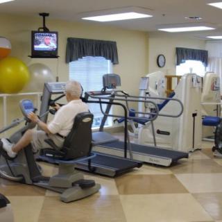 A senior person exercising in a rehabilitation facility equipped with various fitness machines.