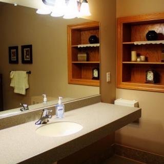 A well-lit bathroom with a mirror, sink, and organized shelves.