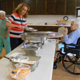 A caregiver serves food to seniors in an assisted living facility, fostering a sense of community and care.