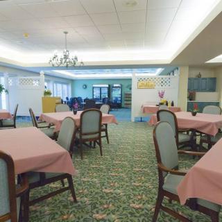 A spacious dining room with neatly arranged tables and chairs, featuring a chandelier and patterned carpet.