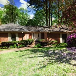 A suburban brick house surrounded by greenery and trees on a sunny day.