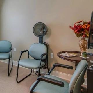 A small waiting room with chairs, a fan, and a table with magazines and flowers.