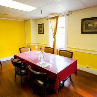 A cozy dining room with yellow walls, a table covered with a red tablecloth, and several chairs.