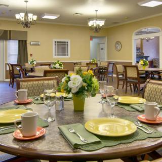 A cozy dining room with neatly arranged tables, set with plates and floral centerpieces.