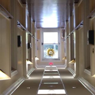 A brightly lit hallway with symmetrical windows and a distant view through a large window at the end.