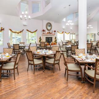 A spacious dining area with elegant decor, featuring multiple tables and chairs arranged on a wooden floor.