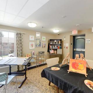 A well-lit art room featuring tables adorned with paintings, a bookshelf, and decorative artwork on the walls.