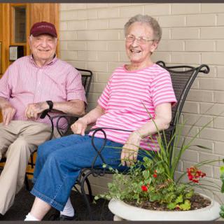 An elderly couple sitting together on a porch, enjoying a peaceful moment outside.