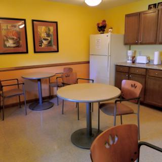 A cozy kitchen and dining area with tables, chairs, a fridge, and colorful artwork on the walls.