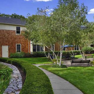 A charming house with a beautifully landscaped garden featuring a walkway, lush lawn, trees, and outdoor seating.