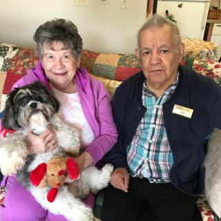 An elderly couple sitting on a couch with their small dog.