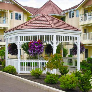 A beautifully decorated gazebo with hanging flowers in a garden setting, surrounded by residential buildings.