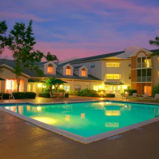 A serene evening view of a hotel with a glowing swimming pool surrounded by illuminated residential buildings.