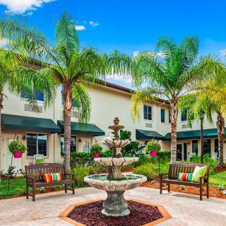A serene courtyard with a central fountain surrounded by palm trees and benches.