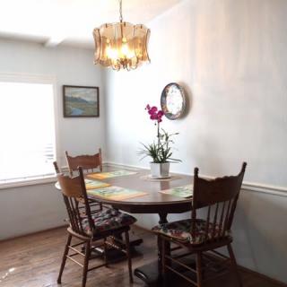 A cozy dining area with a wooden table and chairs, an orchid centerpiece, and a chandelier casting warm light.