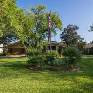 A suburban house with a neatly landscaped front yard featuring a flagpole and surrounding trees.