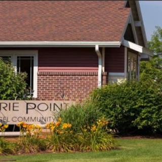 A community sign in front of a brick house with well-maintained landscaping and flowers.