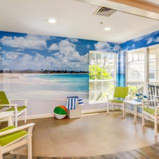 A bright waiting room featuring a beach-themed mural and green-accented chairs.