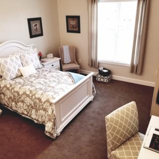 A cozy and well-decorated bedroom with a bed, nightstand, and a window letting in natural light.