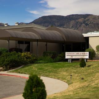 A modern building set against a backdrop of mountains, featuring well-maintained landscaping and a visible sign.