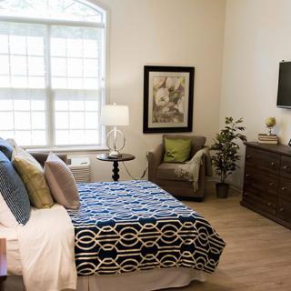 A cozy and well-decorated bedroom with a modern interior design, featuring a comfortable bed, armchair, dresser, and decorative elements.