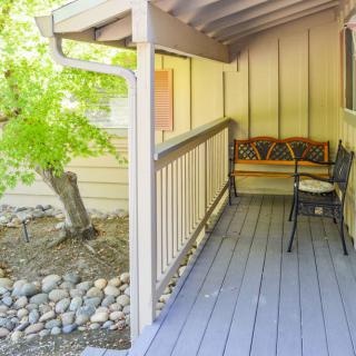 A cozy covered porch with a wooden bench and chairs overlooking a garden.