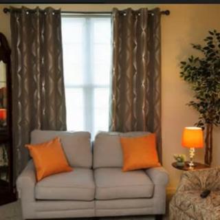 A cozy living room with a gray sofa, orange pillows, patterned curtains, and warm lighting.