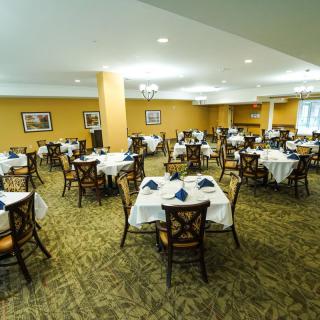 An elegant dining area with neatly arranged tables and chairs, each adorned with white tablecloths and blue napkins.