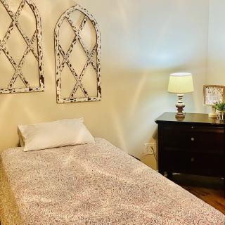 A cozy bedroom with a single bed and nightstand, featuring decorative wall art and a lit lamp.