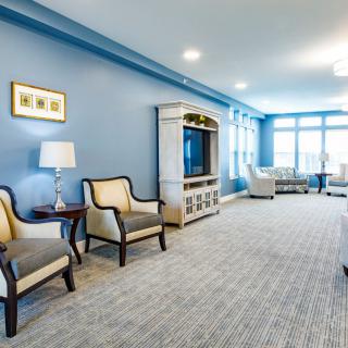 A spacious living room with blue walls, featuring comfortable chairs, a television, and ample natural light.