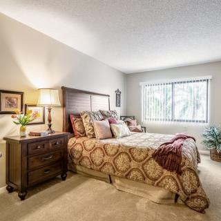 A cozy and elegantly decorated bedroom featuring a large bed with patterned bedding, a wooden nightstand with a lamp, and a window allowing natural light to fill the room.