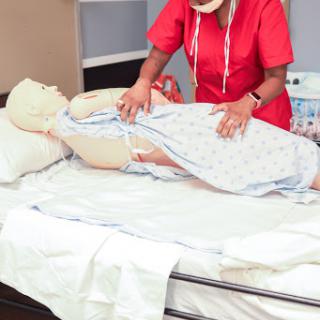A healthcare professional demonstrating patient care techniques using a training mannequin in a medical setting.